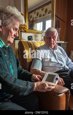 In prossimità della coppia di anziani controllare il proprio sangue-pressione utilizzando un digital monitor della pressione del sangue nel salotto di casa Foto Stock