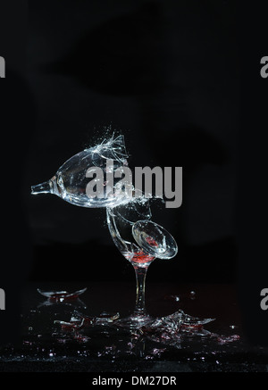 Smashing bicchieri di vino su un buio riflettente sfondo nero rotto i frammenti di vetro battenti come le linee di frattura si diffondono attraverso Foto Stock