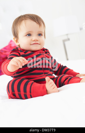 Bambino seduto sul letto indossando pigiami Foto Stock