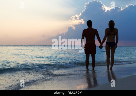 Silhouette di giovane camminando lungo la spiaggia al tramonto Foto Stock