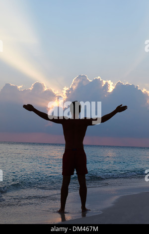 Silhouette di uomo con le braccia tese sulla spiaggia al tramonto Foto Stock
