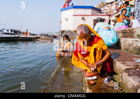 Donne puja illuminazione candele e balneazione nel fiume Gange, Varanasi, India Foto Stock