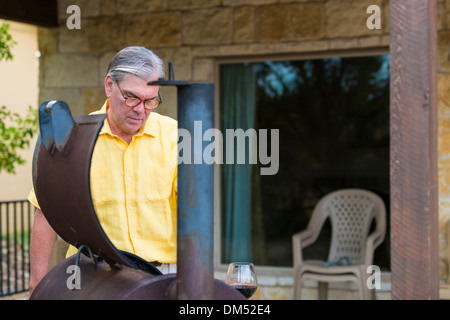 Voce maschile senior citizen di etnia caucasica, 60 anni, sta preparando il barbecue smoker pit per grigliare. Texas, Stati Uniti d'America Foto Stock