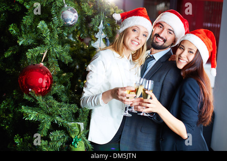 Ritratto di gioiosa colleghi in Santa caps bevendo champagne da albero di Natale Foto Stock
