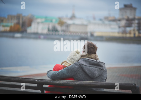 Vista posteriore di affettuosa giovane seduto sul banco e guardando il fiume Foto Stock