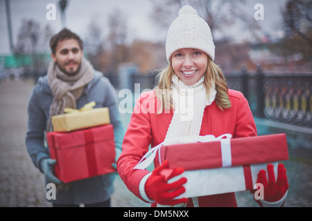 Immagine di felice ragazza giovane con giftboxes guardando la fotocamera con il suo fidanzato dietro Foto Stock