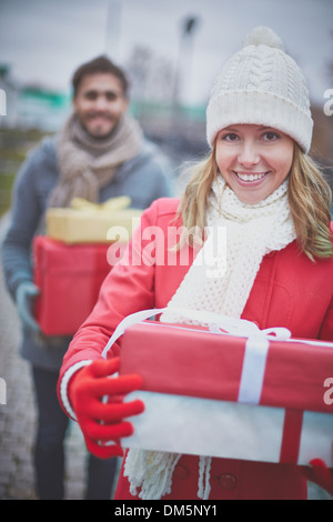 Immagine di felice ragazza giovane con giftboxes guardando la fotocamera con il suo fidanzato dietro Foto Stock