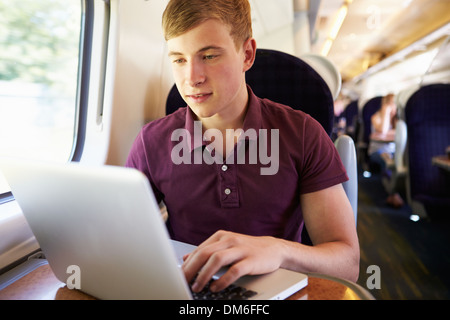 Giovane uomo utilizzando laptop in viaggio in treno Foto Stock