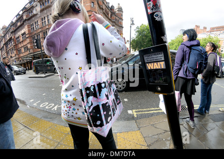 Londra, Inghilterra, Regno Unito. Giovane donna in attesa in corrispondenza di un passaggio pedonale Foto Stock