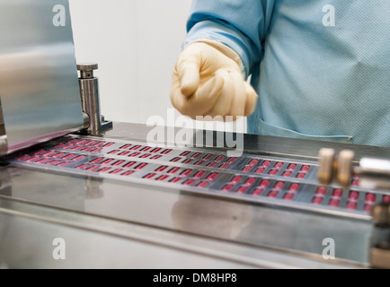 Produzione farmaceutica con la macchina blisteratrice e mano umana in guanti Foto Stock