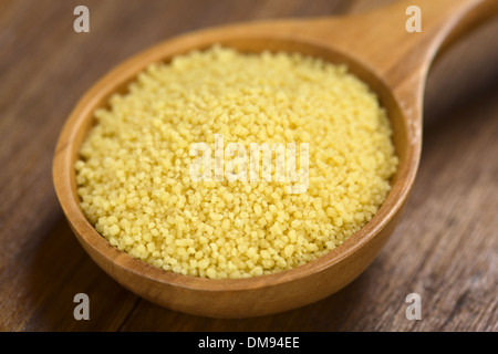 Couscous crudo sul cucchiaio di legno (molto leggera profondità di campo e la messa a fuoco di un terzo nel cuscus) Foto Stock