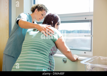 L'infermiera consolante teso incinta a finestra nella stanza di ospedale Foto Stock