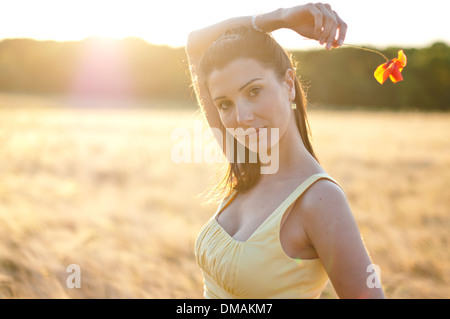 Giovane donna in abito in piedi in un campo di grano al tramonto Foto Stock