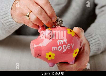 Primo piano di un uomo persona che mette denaro denaro denaro monete monete monete in salvadanaio concetto di risparmio pensione investimento Inghilterra Regno Unito Regno Unito Gran Bretagna Foto Stock