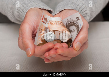 Primo piano mano di uomo persona mani che tengono in mano denaro inglese banconota da dieci sterline e monete in contanti risparmi Inghilterra Regno Unito Regno Unito Gran Bretagna Foto Stock