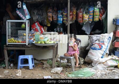 Phnom Penh Cambogia. Decimo Dec, 2013. Una ragazza si siede di fronte a un negozio di alimentari in Chhba Anmpov baraccopoli sui motivi di un cimitero Cinese in Phnom Penh Cambogia, 10 dicembre 2013. La Cambogia è uno dei venti paesi con i più alti tassi di malnutrizione tra i bambini. Circa 670.000 orfani vive in Cambogia. Ogni 22 bambino muore nel primo anno di vita. Più di un terzo della popolazione vive con meno di un dollaro al giorno. Foto: Jens Kalaene/dpa/Alamy Live News Foto Stock