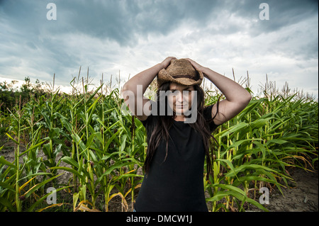 Donna in piedi nel campo di mais indossando cappello di paglia sotto il cielo in tempesta Foto Stock