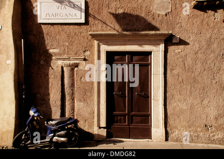 Uno scooter parcheggiato accanto a una porta di legno con un antica colonna incassata in una parete dietro, via Margana, Roma Italia. Foto Stock