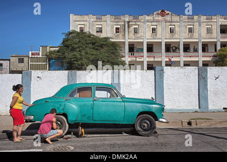 La riparazione di una vecchia auto di fronte a una scuola primaria, STREET AMBIANCE, CIENFUGOS, ex PORT città popolata dai francesi nel XIX secolo, elencato come un sito del patrimonio culturale mondiale dell UNESCO, CUBA, CARAIBI Foto Stock