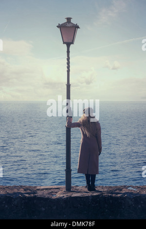 Una donna in un cappotto rosa è in piedi accanto a una lanterna a mare Foto Stock