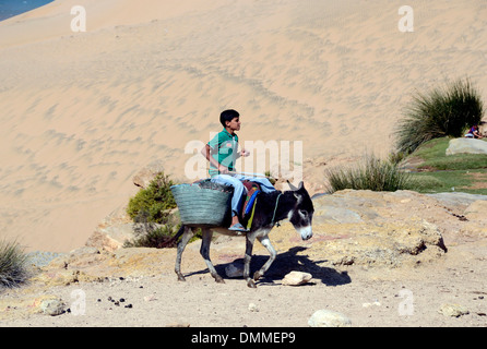 Berber boy cavalcando un asino una piccola valle vicino a un villaggio berbero sulla costa a sud di essaouira marocco Foto Stock