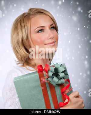 Ritratto di donna graziosa cercando nel lato sul grigio sfondo innevato, tenendo le mani in confezione regalo, vacanze invernali concept Foto Stock