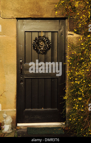 Ghirlanda di Natale appeso sulla porta anteriore di un flagello cottage' fiancheggiata da fioritura invernale gelsomino, Eyam; Derbyshire, Regno Unito Foto Stock