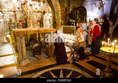 Pellegrini cristiani coda sul loro ginocchia preparando a toccare e pregare per la roccia del Calvario nella Cappella della Crocifissione. Foto Stock