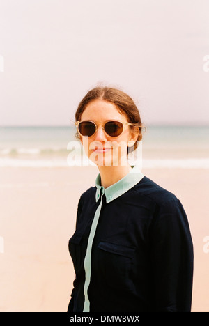 Una donna che indossa gli occhiali da sole su di una spiaggia. Foto Stock