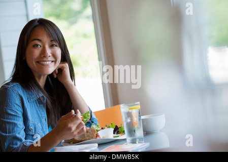 Una donna seduta a mangiare in un bar. Foto Stock