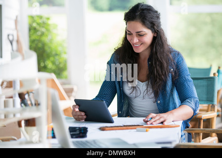 Una donna che lavora in una tabella utilizzando una tavoletta digitale. Foto Stock