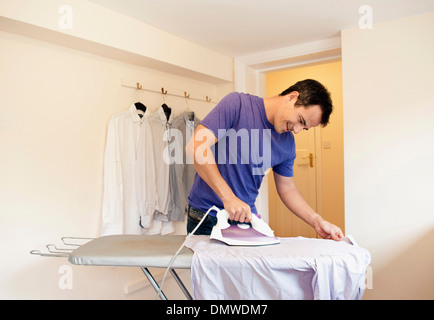 Un uomo a stirare una maglietta sulla tavola da stiro. Foto Stock