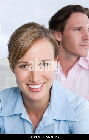 Una giovane coppia di una donna in primo piano sorridente e un uomo cercando in distanza. Foto Stock