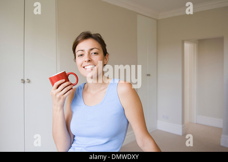 Una donna che indossa un blu in alto seduto tenendo un red china mug. Foto Stock