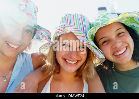 Tre giovani ragazze in una fila indossando sunhats guardando la fotocamera e sorridente. Foto Stock