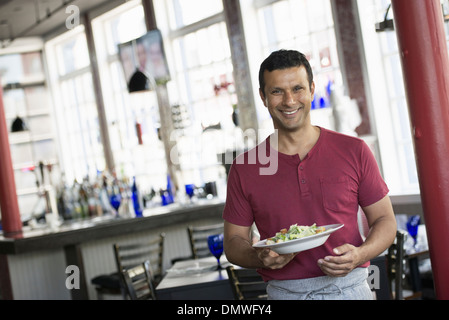 Un bar interno. Un uomo in un cameriere il grembiule di servire un pasto. Foto Stock