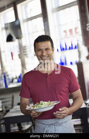 Un bar interno. Un uomo in un cameriere il grembiule di servire un pasto. Foto Stock