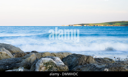 Una scena di mare con scogli in primo piano e il vecchio Harry's rocks in distanza nella calda luce della sera. Foto Stock