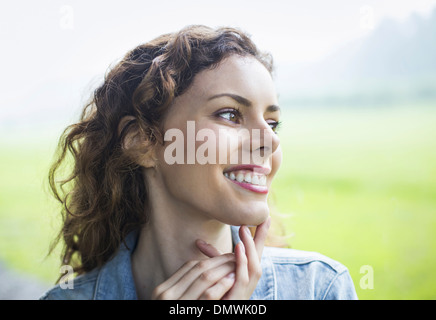 Una giovane donna in un paesaggio rurale con battente capelli ricci. Guardando lontano in distanza. Foto Stock