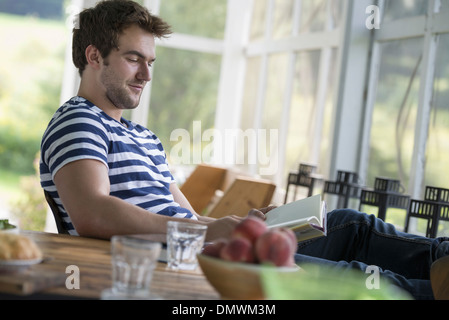 Un uomo seduto a un tavolo di lettura di un libro. Foto Stock