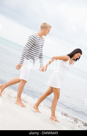 Caucasian felice coppia giovane tenendo le mani mentre si cammina a piedi nudi sulla spiaggia in una romantica destinazione di viaggio Foto Stock