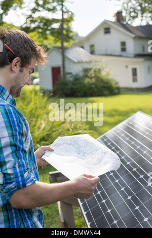 Un uomo con un piano per collocare un pannello solare in un casale giardino. Foto Stock