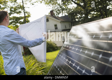 Un uomo con un piano per collocare un pannello solare in un casale giardino. Foto Stock