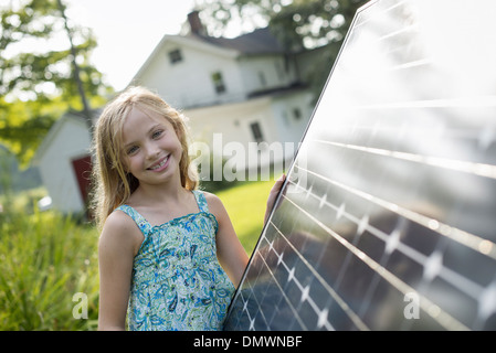 Una giovane ragazza accanto a un grande pannello solare in un casale giardino. Foto Stock