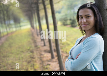 Una donna con le braccia incrociate appoggiata contro un albero. Foto Stock