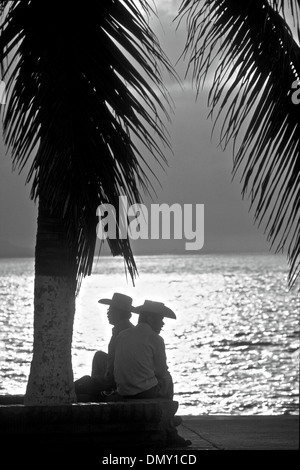 Due uomini seduti vicino alla spiaggia al tramonto in Acapulco, Messico Foto Stock