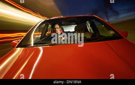 Un uomo alla guida di una macchina di notte su una strada rettilinea. Foto Stock