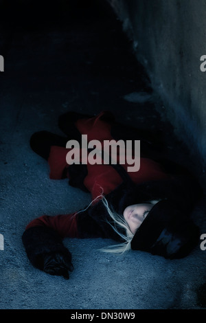 Una donna in un rivestimento di colore rosso è giacente in un buio del tunnel Foto Stock