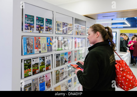 Una donna esplora le informazioni turistiche di opuscoli nel visitare Belfast centro informazioni turistiche Foto Stock