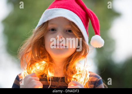 Una bambina vestita di un cappello da Babbo Natale e la Fata le luci di Natale Foto Stock